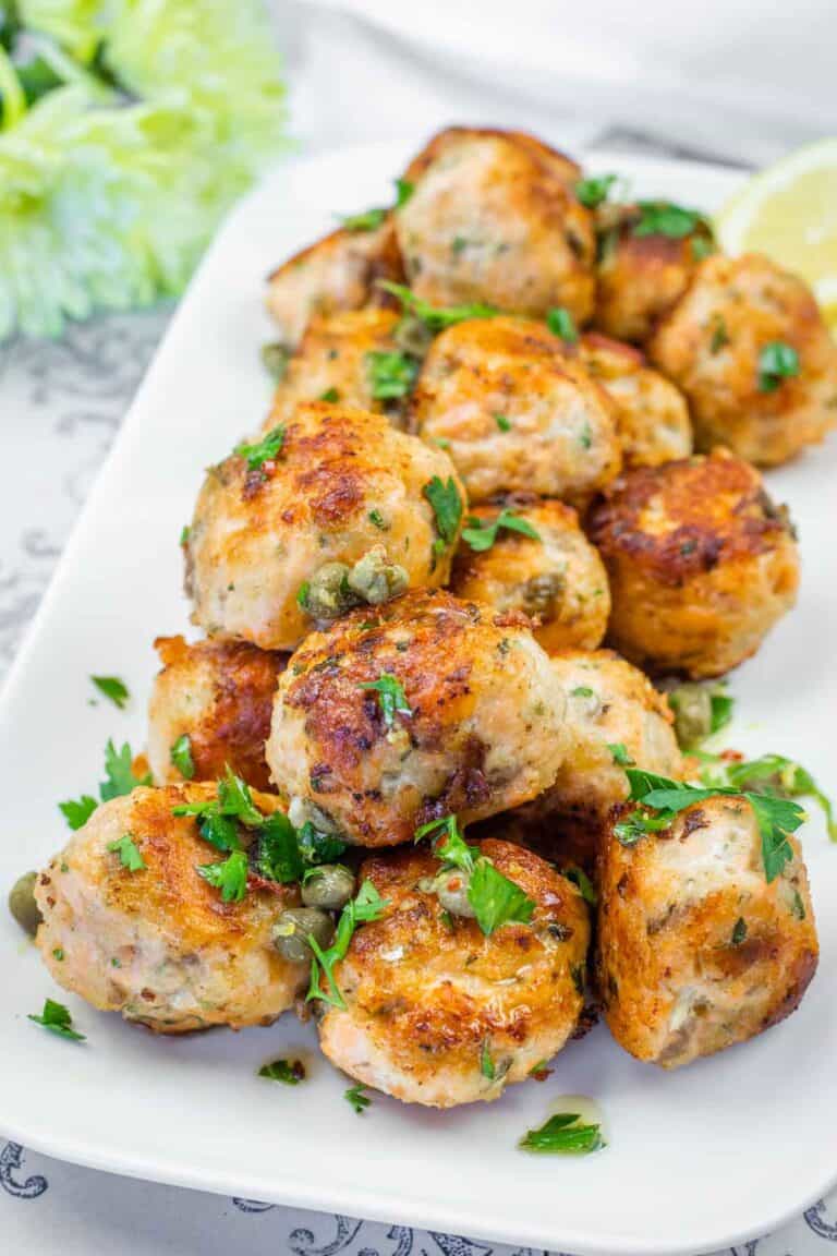 A pile of golden-brown salmon balls garnished with fresh parsley, capers, and lemon wedges on a white plate.