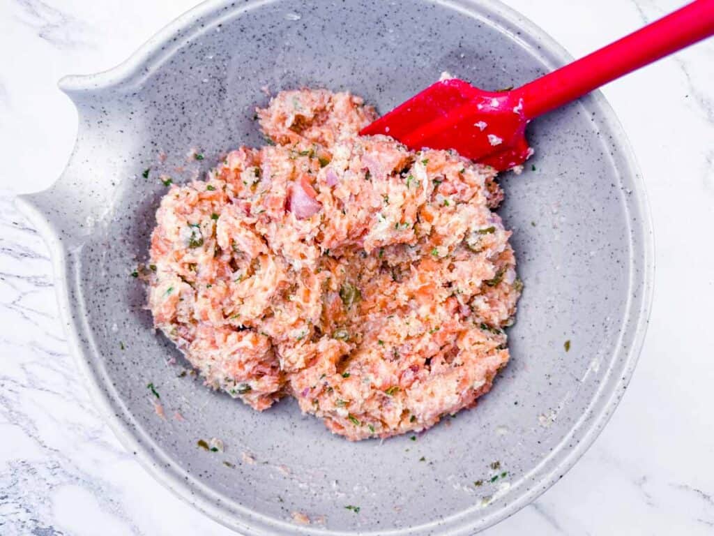 Overhead shot of raw salmon mixture being stirred with a red spatula in a gray bowl.