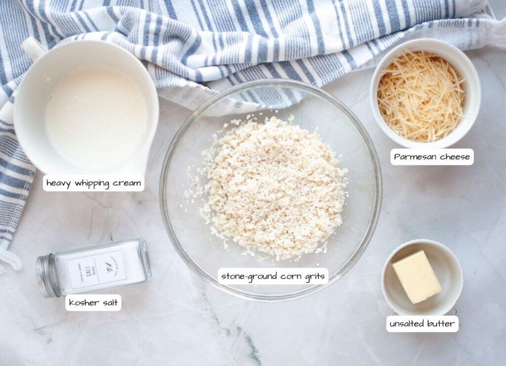 Overhead shot of labeled ingredients for stone ground corn grits: grits, heavy cream, Parmesan cheese, unsalted butter, and kosher salt.