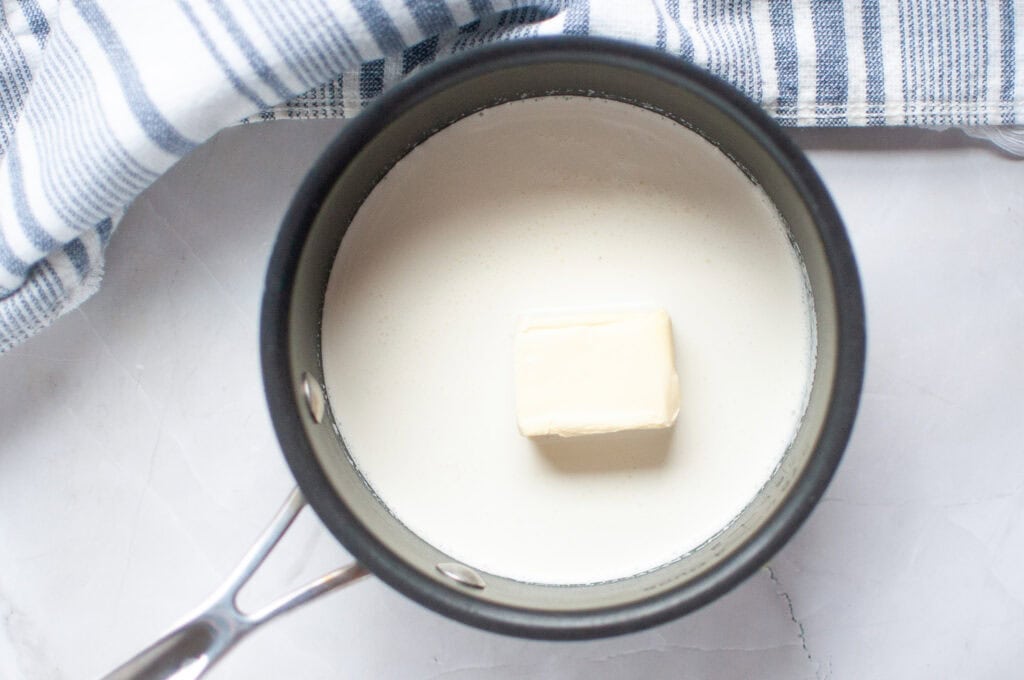 Overhead shot of a pat of butter melting in a saucepan of white milk.