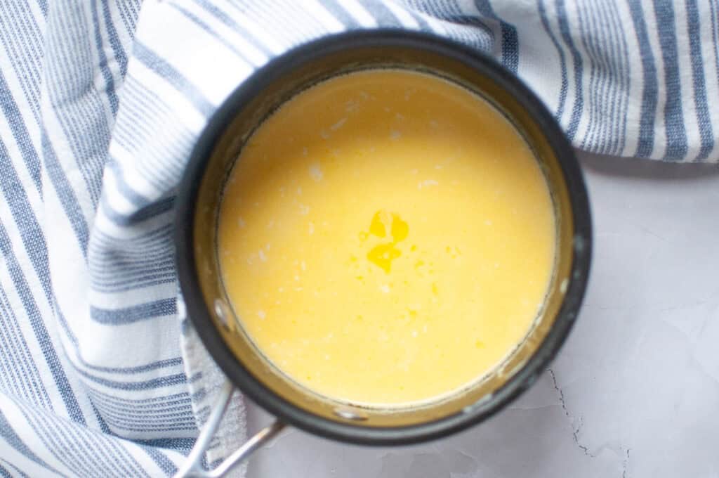 Overhead shot of a saucepan containing a smooth, pale yellow Hollandaise sauce with melted butter.