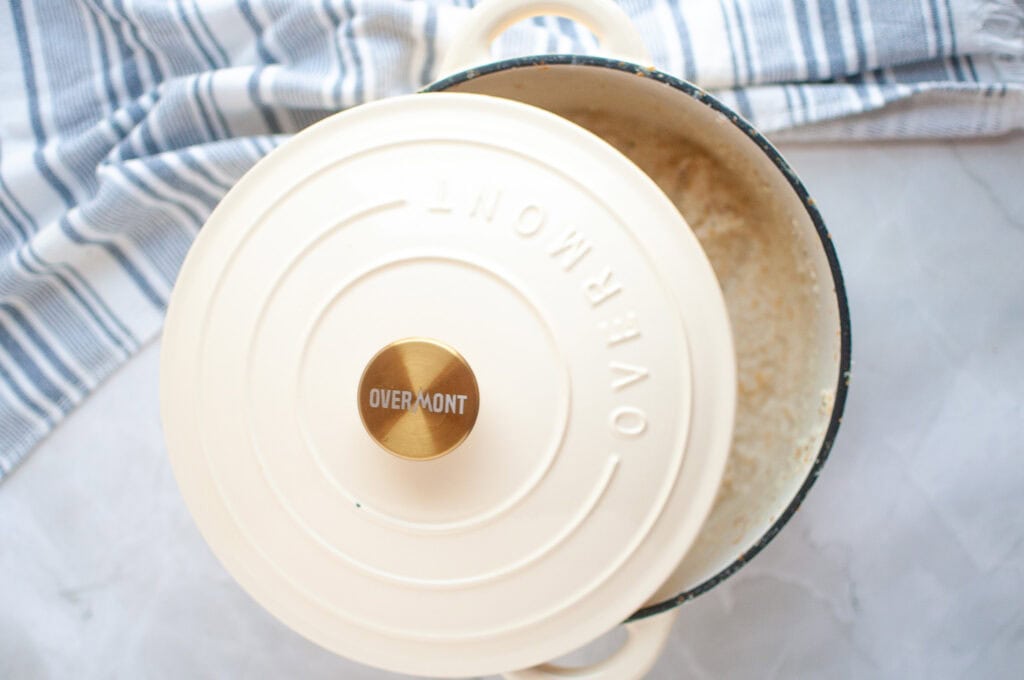 Overhead shot of cooked corn grits in a white Overmont enameled cast iron pot with the lid partially off.
