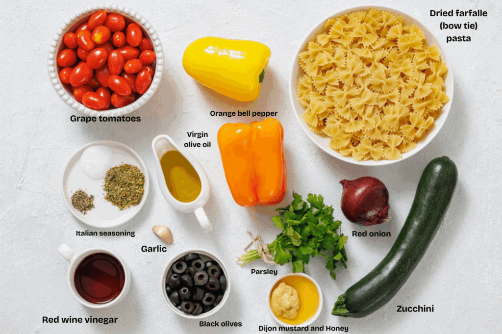 Bow tie pasta, grape tomatoes, yellow bell peppers, red onion, zucchini, black olives, garlic, parsley, olive oil, red wine vinegar, Dijon mustard, honey, and Italian seasoning displayed.