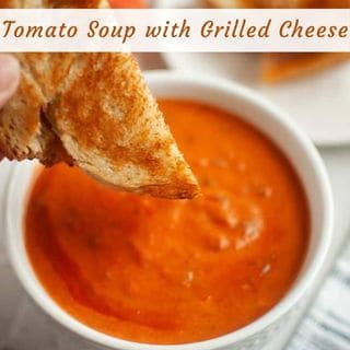 A bowl of tomato soup with a grilled cheese sandwich being dipped into it.