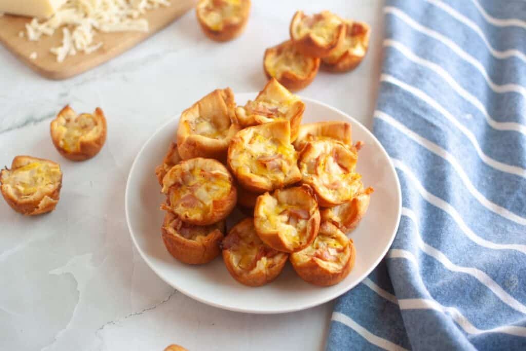 A white plate piled with small, golden-brown ham & cheese puffs.