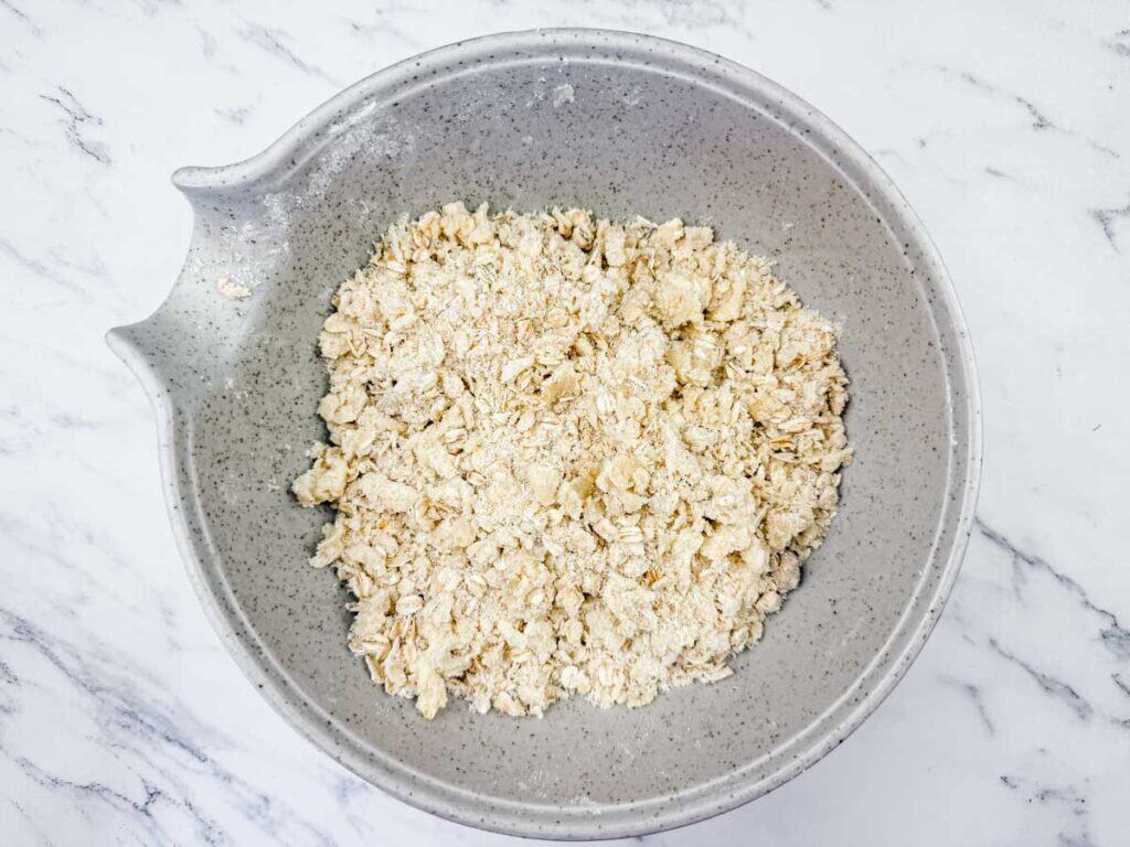 Overhead shot of a gray mixing bowl filled with a light-colored, coarse crumbly mixture, likely for a fruit dessert.