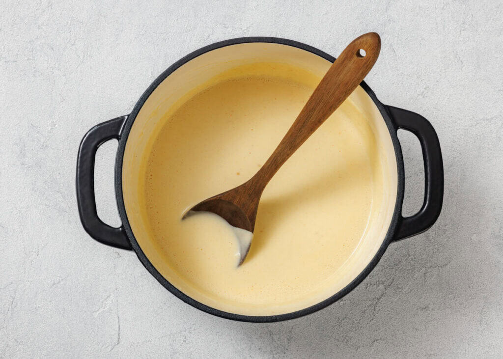 A pot filled with a creamy yellow sauce, with a wooden spoon resting inside, sits on a light gray surface.