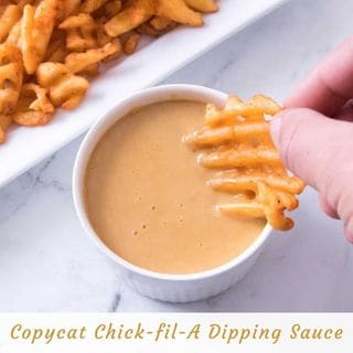 A hand dips a waffle fry into a small white bowl of creamy, light orange dipping sauce. In the background, a white rectangular plate holds more waffle fries. The text "Copycat Chick-fil-A Dipping Sauce" is overlaid at the bottom.