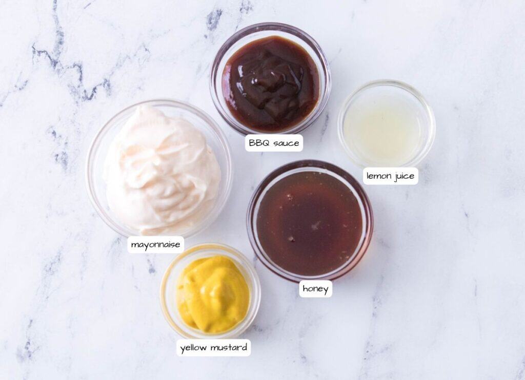Five glass bowls on a marble surface containing mayonnaise, BBQ sauce, lemon juice, honey, and yellow mustard, each labeled with text.