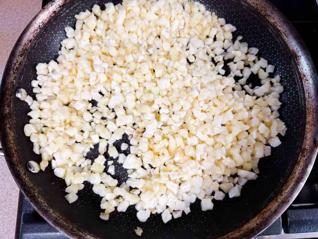Diced white vegetables cooking in a black frying pan on a stovetop.