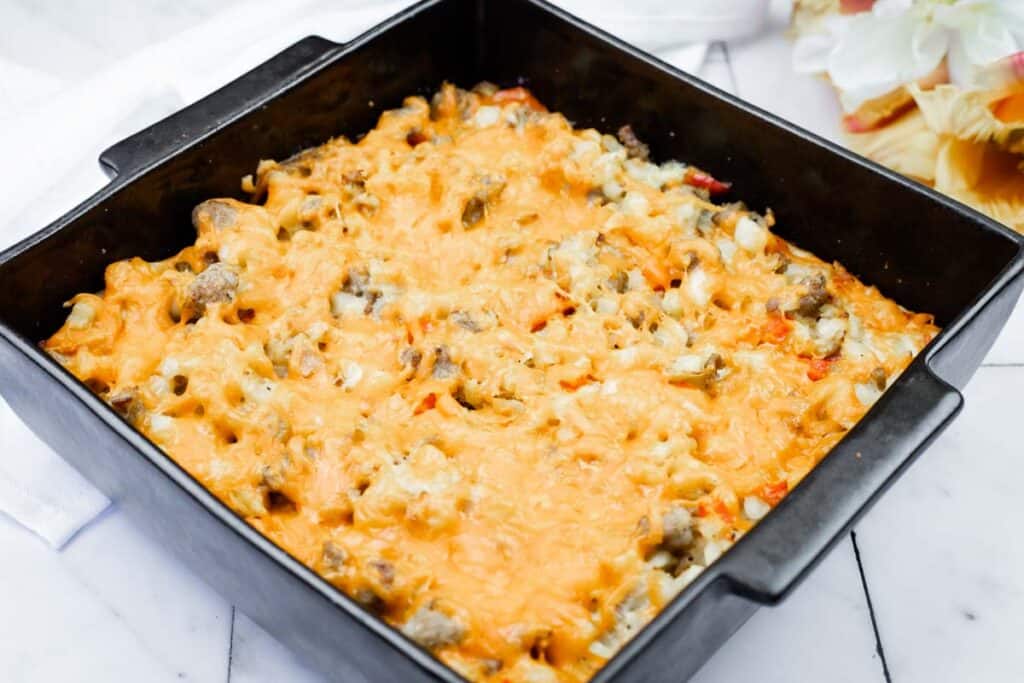 A black square baking dish filled with a baked casserole topped with melted cheese, ground meat, and vegetables, set on a white surface.