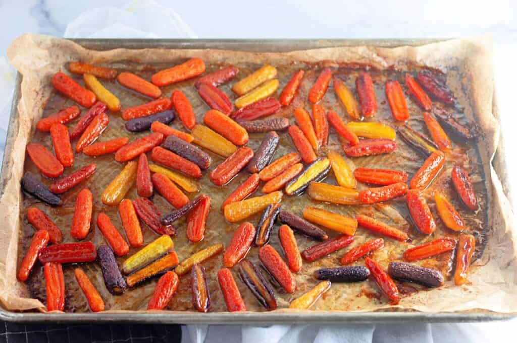 A baking sheet lined with parchment paper holds roasted baby carrots in orange, yellow, and purple varieties.