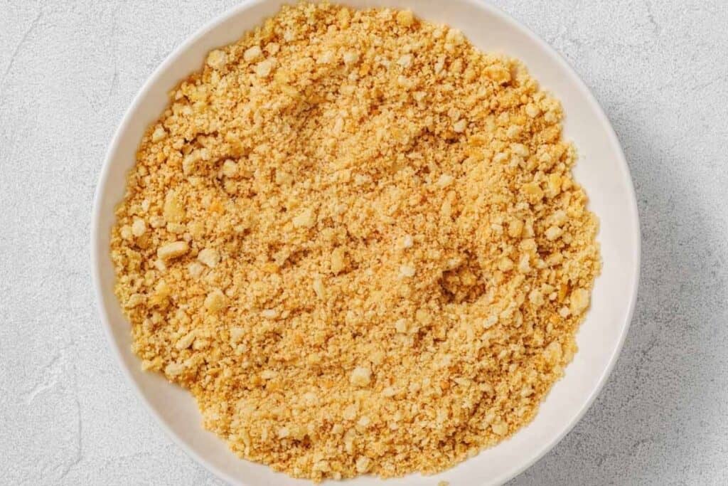 A white bowl filled with finely crushed graham cracker crumbs sits on a light gray surface.