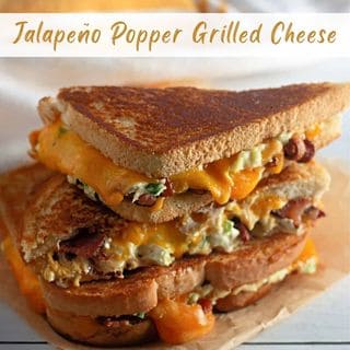 A stack of two golden-brown grilled cheese sandwiches with melted orange cheese and green jalapeño pieces, served on brown parchment paper.