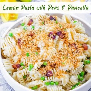 A white bowl is filled with creamy lemon pasta, green peas, and diced pancetta, topped with golden breadcrumbs and garnished with parsley, on a blue wooden table.