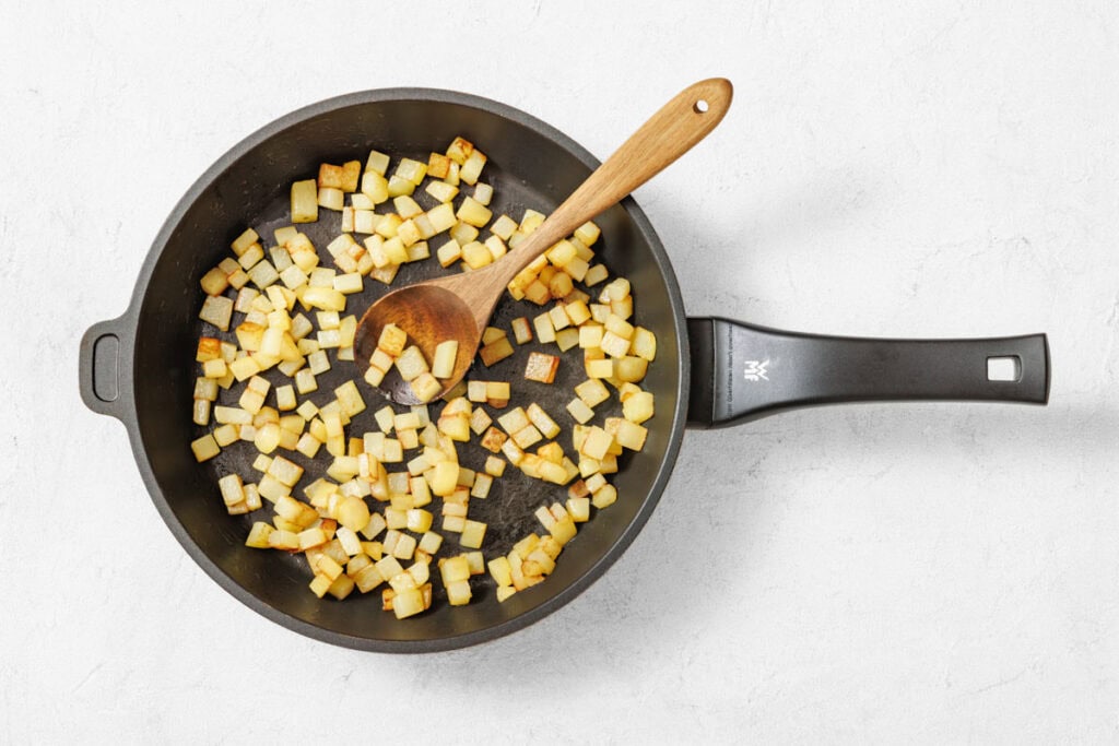 Overhead shot of a black nonstick skillet filled with golden-brown diced potatoes and a wooden spoon.