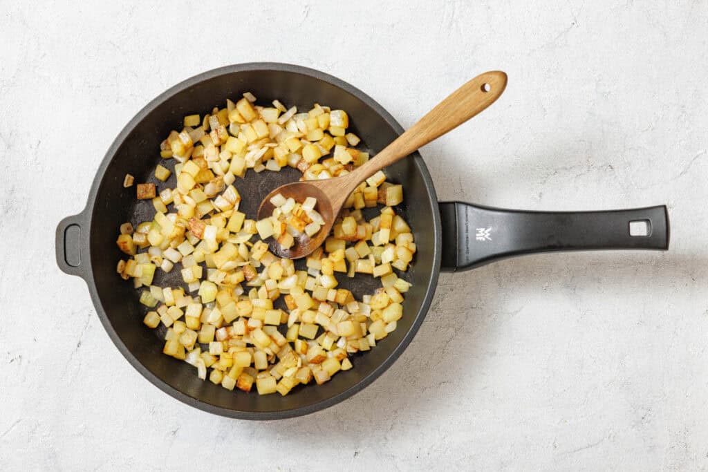 Overhead shot of a black nonstick skillet filled with golden-brown diced potatoes and a wooden spoon.