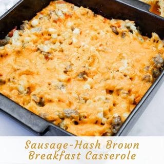 A close-up, slightly high-angle shot of a square black plate holding a golden-brown serving of Sausage-Hash Brown Breakfast Casserole, featuring visible sausage, potatoes, and melted orange cheese, garnished with fresh green parsley, with a black fork to the right.
