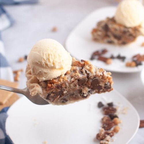 A fork holds a slice of pie topped with a scoop of vanilla ice cream; more pie slices are visible on plates in the background.