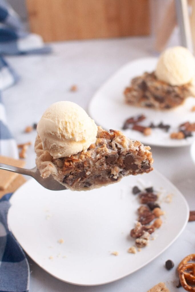 A fork holds a slice of pie topped with a scoop of vanilla ice cream; more pie slices are visible on plates in the background.