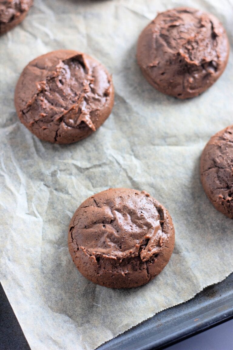 Three chocolate cookies on parchment paper, resting on a baking tray.