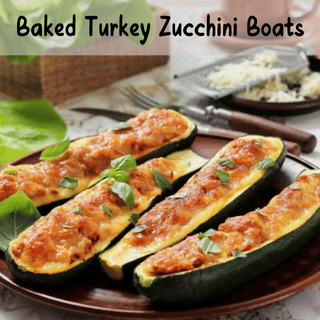 Four zucchini halves stuffed with baked turkey mixture, topped with herbs, served on a brown plate with a fork, knife, and a small bowl of grated cheese in the background.