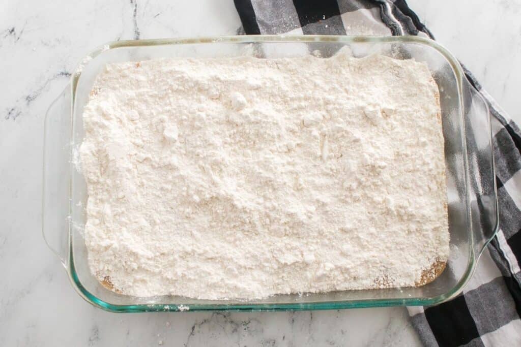 A glass baking dish filled with a dessert topped with a layer of powdered sugar, set on a marble surface next to a black and white checkered cloth.
