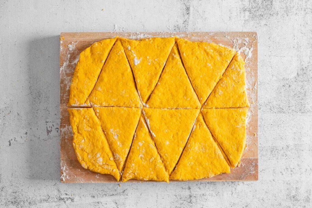 A rectangular sheet of orange dough on a floured wooden board, cut into triangles and rectangles, ready for baking.