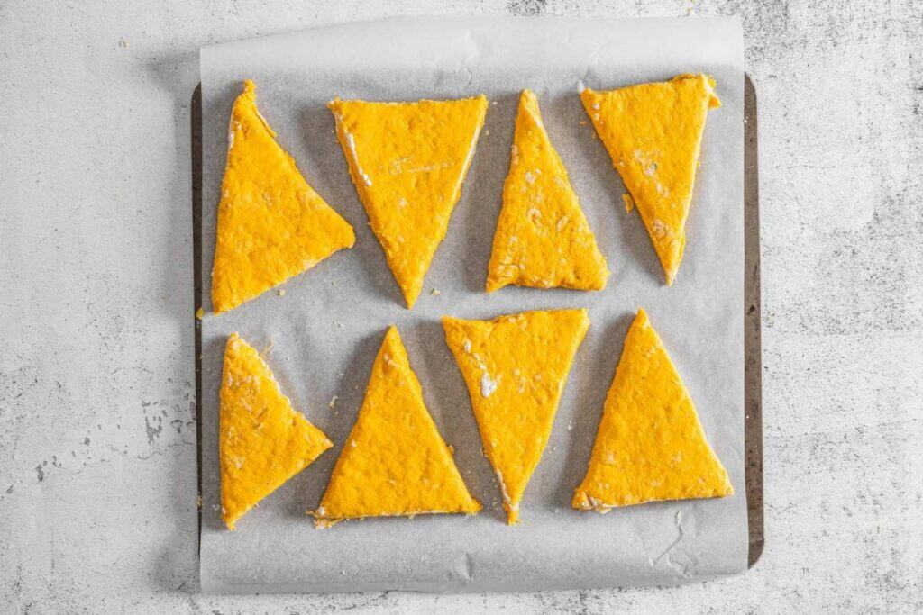 Eight triangular pieces of orange dough are arranged on a parchment-lined baking sheet, ready to be baked.