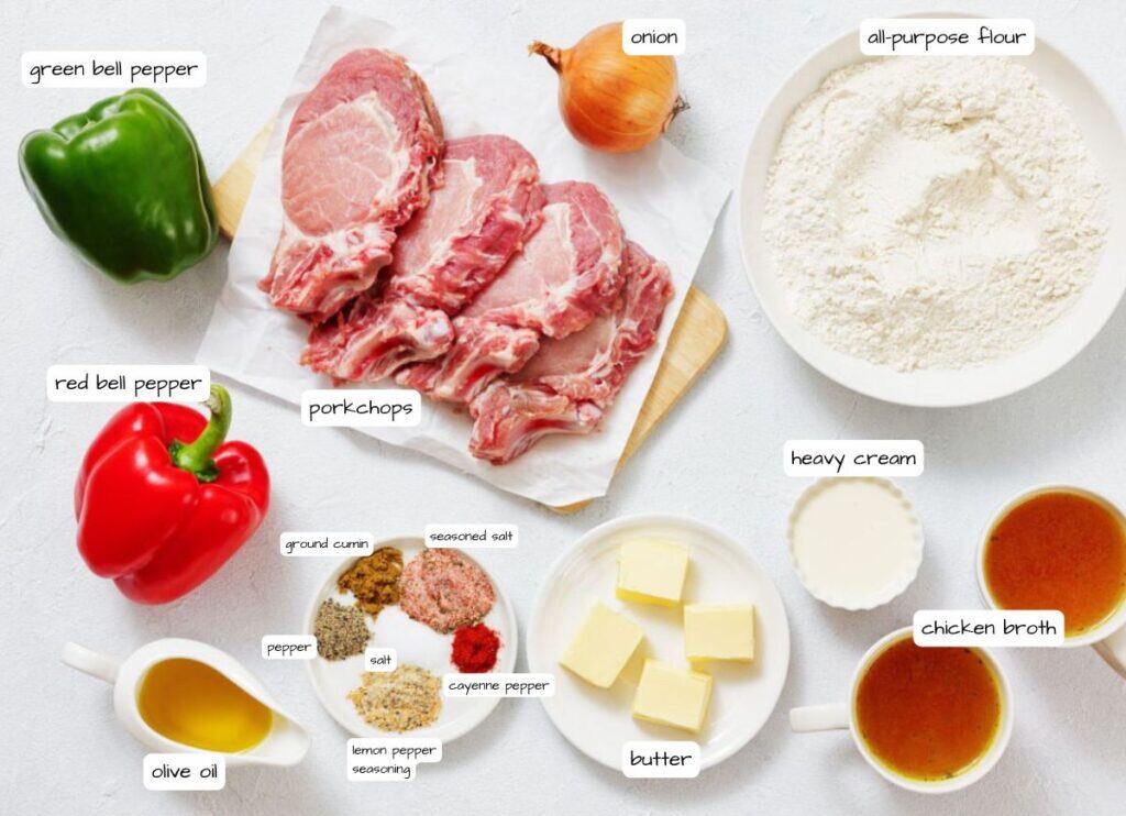 Raw pork chops, green and red bell peppers, onion, all-purpose flour, heavy cream, chicken broth, butter, olive oil, and various spices arranged on a white surface.