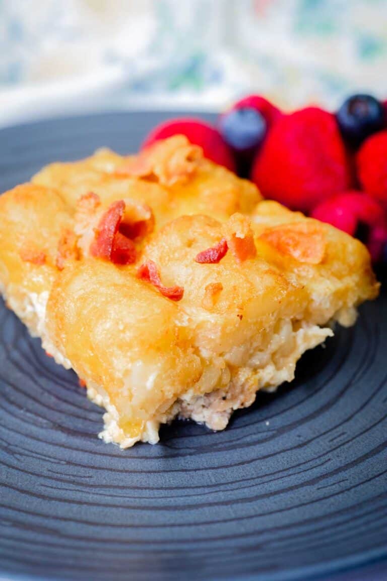 A serving of tater tot casserole with bacon bits on a black plate, accompanied by a side of mixed berries.