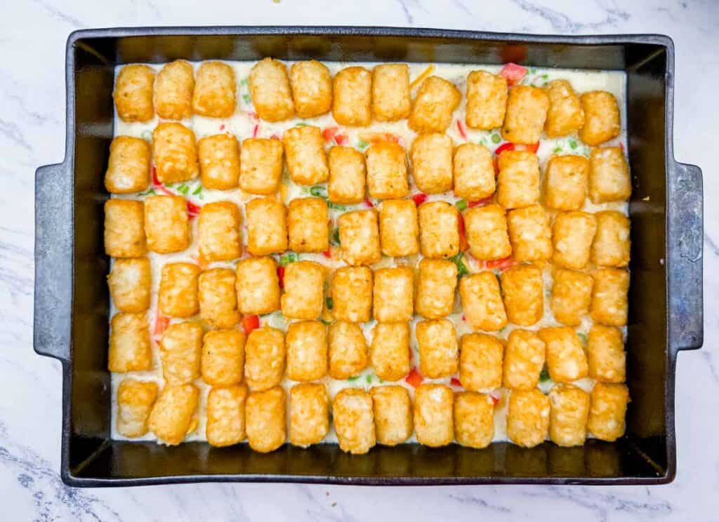 A rectangular baking dish filled with a casserole, topped with evenly arranged golden tater tots over a creamy mixture with visible vegetables.