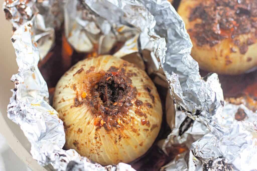 A whole onion stuffed with a spice mixture, baked in aluminum foil with visible seasonings and juices.