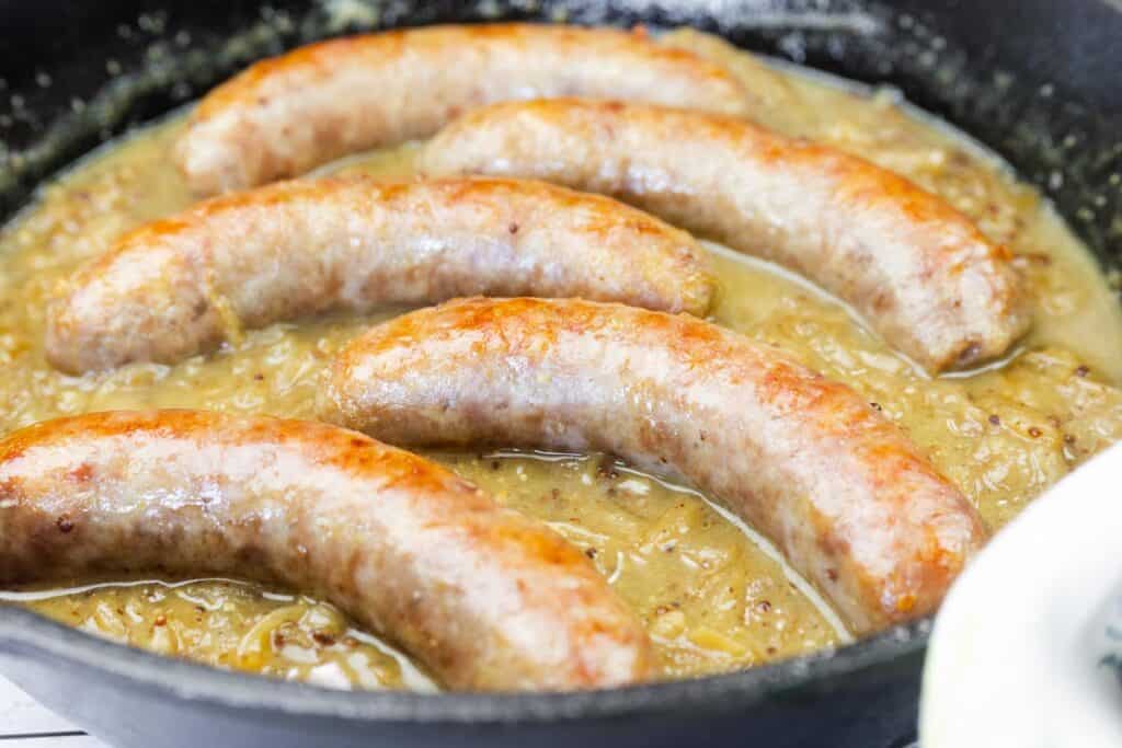 Five browned sausages simmering in a pan filled with onion gravy.
