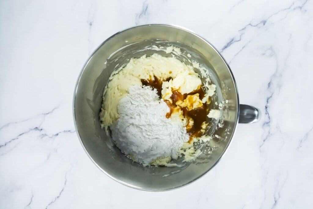 Frosting mixture with powdered sugar, vanilla, and caramel sauce in a mixing bowl.