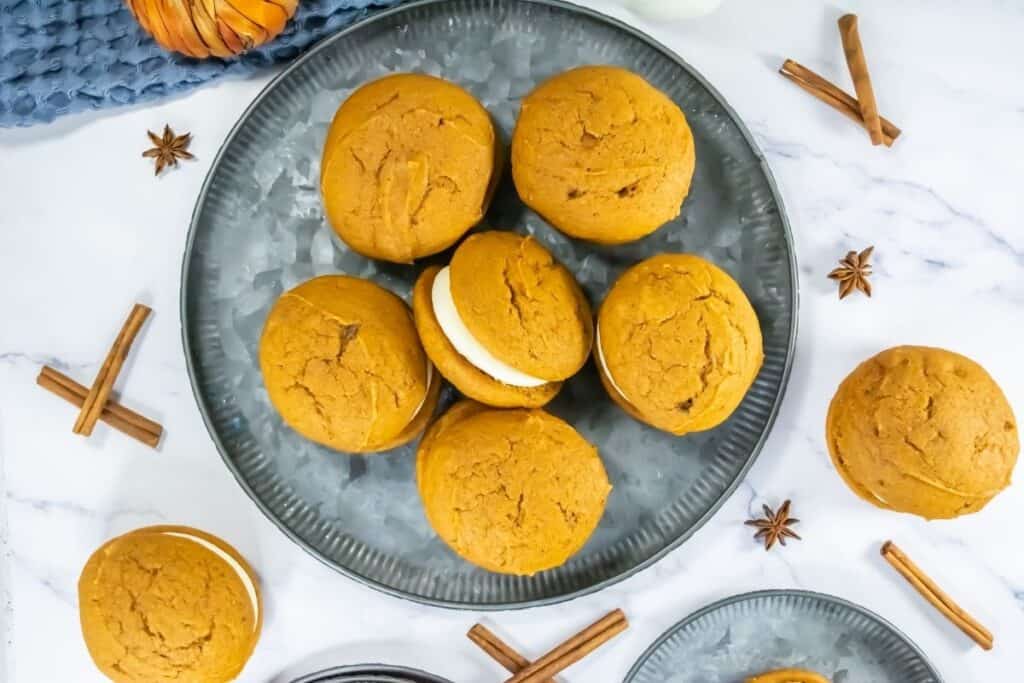Plate of pumpkin whoopie pies filled with cream frosting, surrounded by cinnamon sticks and star anise.