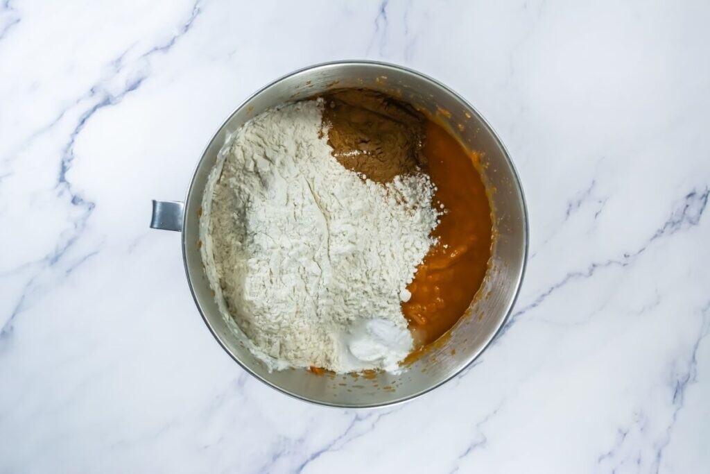 Mixing bowl with pumpkin batter ingredients, including flour, salt, baking soda, baking powder, and pumpkin pie spice before blending.