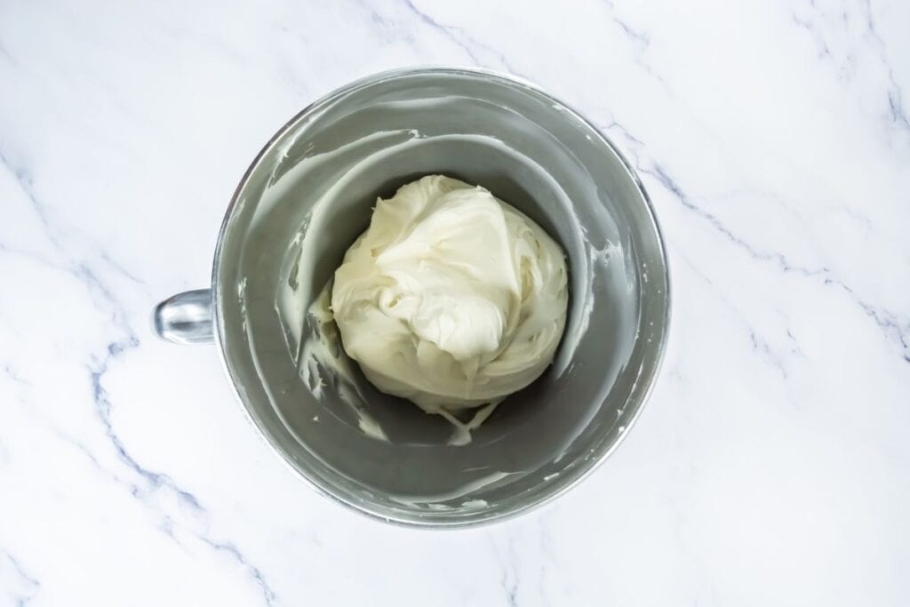 Bowl of smooth cream cheese frosting in a metal mixing bowl on a marble surface.
