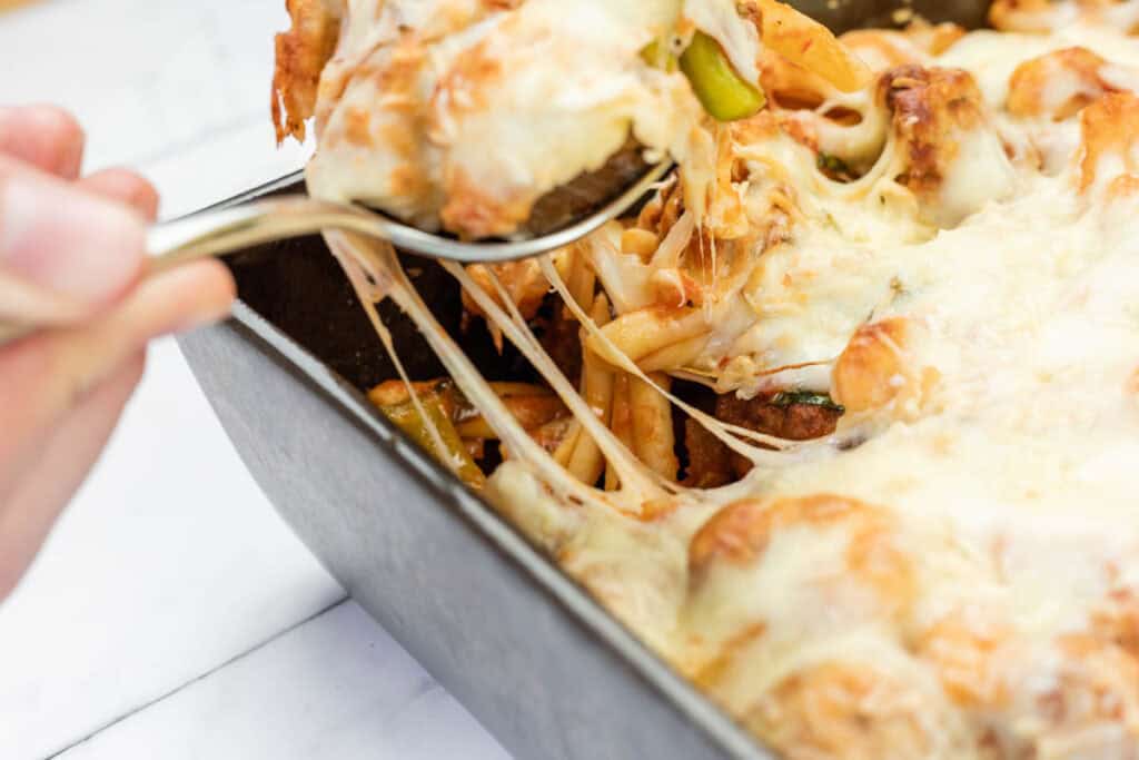 A hand lifts a spoonful of Cheesy Meatball Casserole from the casserole.