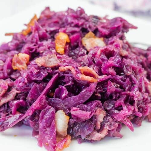 A plate of cooked red cabbage mixed with pieces of bacon, served on a white dish.