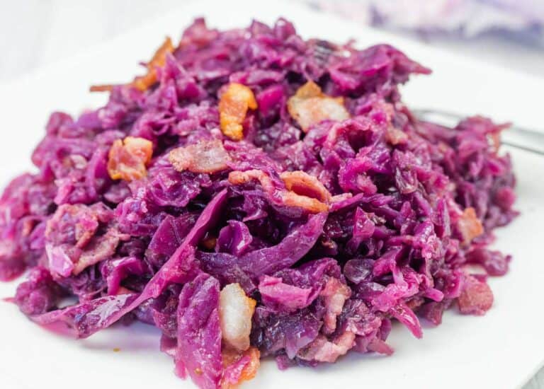 A plate of cooked red cabbage mixed with pieces of bacon, served on a white dish.