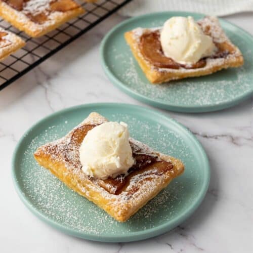Buttery apple tart slices with vanilla ice cream on turquoise plates, dusted with powdered sugar, modern dessert presentation.