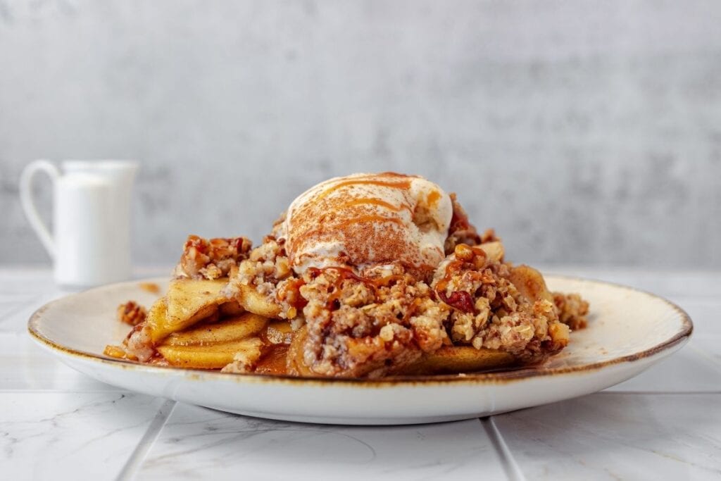 Sweet apple pie with crumb topping and vanilla ice cream on a rustic plate