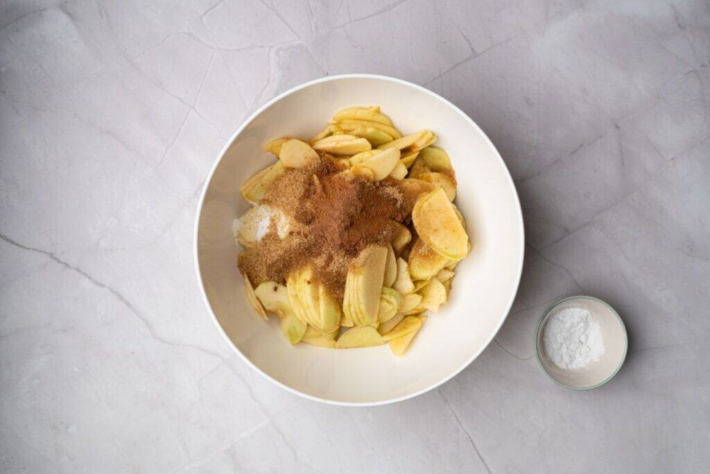 Sweet potato wedges with cinnamon and sugar in a white bowl on a marble surface.