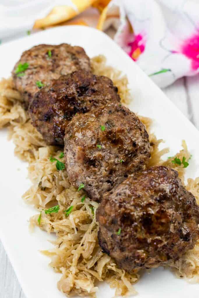 Four browned meat patties are served on a bed of shredded cabbage, garnished with chopped parsley, on a white rectangular plate.