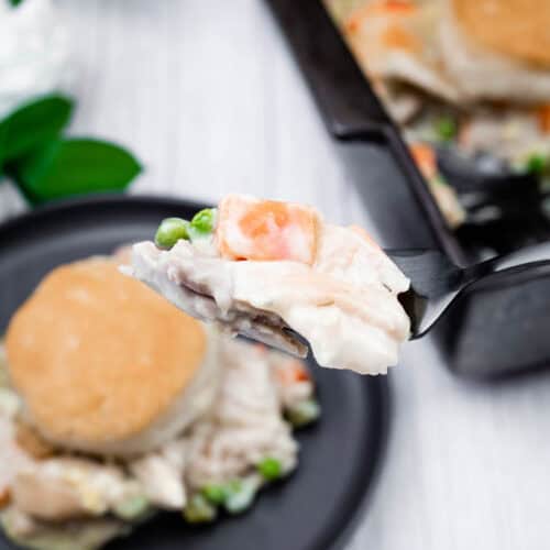 Creamy chicken pot pie filling with peas on spoon, savory comfort food close-up.