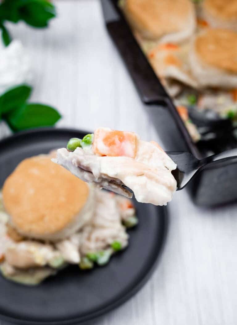 Creamy chicken pot pie filling with peas on spoon, savory comfort food close-up.