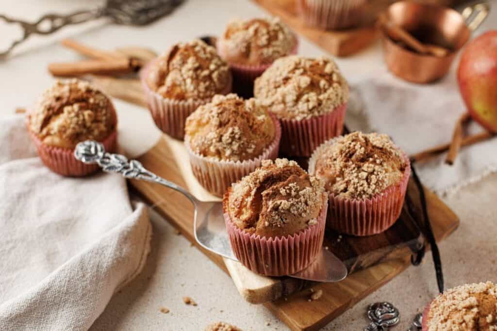 Delicious apple cinnamon muffins in pink baking cups on wooden tray.