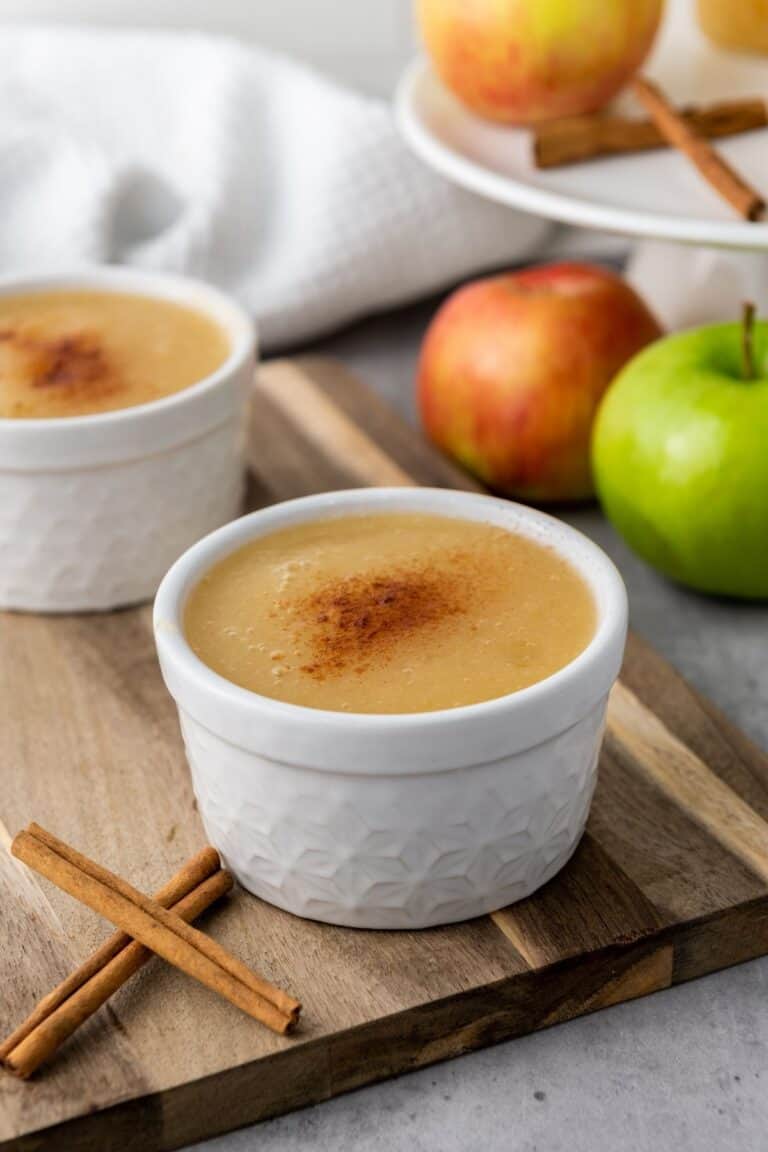 Creamy caramel custard dessert served in white textured ramekins with apples and cinnamon sticks.