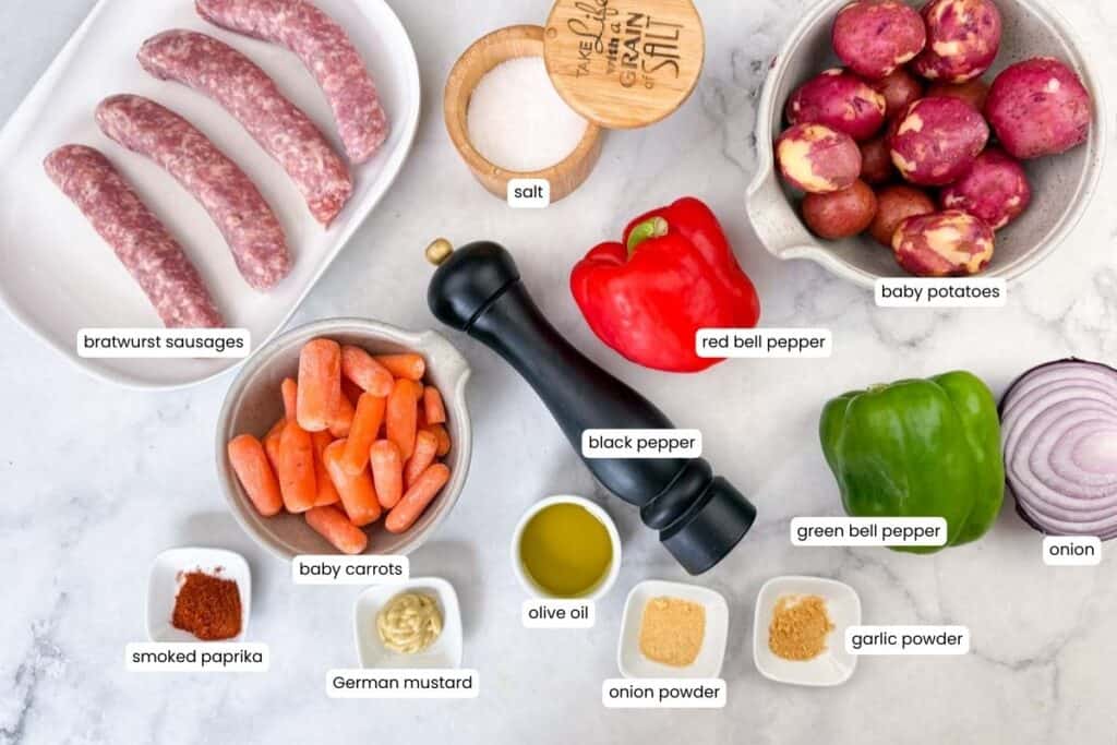 Labeled ingredients for sheet pan bratwurst and potatoes, including sausages, baby potatoes, carrots, peppers, onion, and spices.